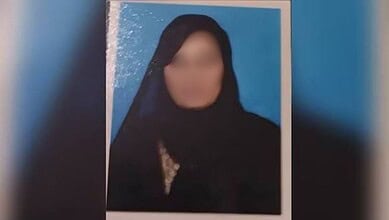 Blurry photo of a woman wearing a black headscarf against a blue background.