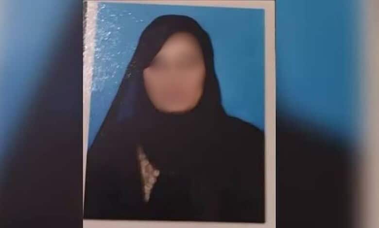 Blurry photo of a woman wearing a black headscarf against a blue background.