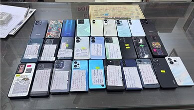 Collection of various smartphones displayed on a glass table with notes attached to each device.