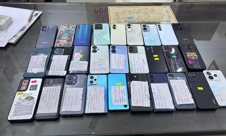 Collection of various smartphones displayed on a glass table with notes attached to each device.