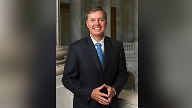 Senator Lindsey Graham in a suit smiling outdoors in front of columns.