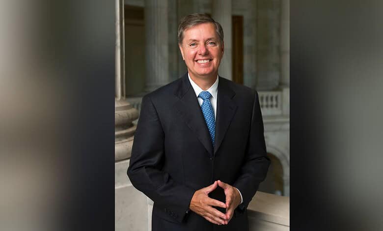 Senator Lindsey Graham in a suit smiling outdoors in front of columns.