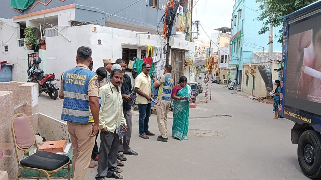 Group of people gathered on a street in Hyderabad, some wearing city police vests.