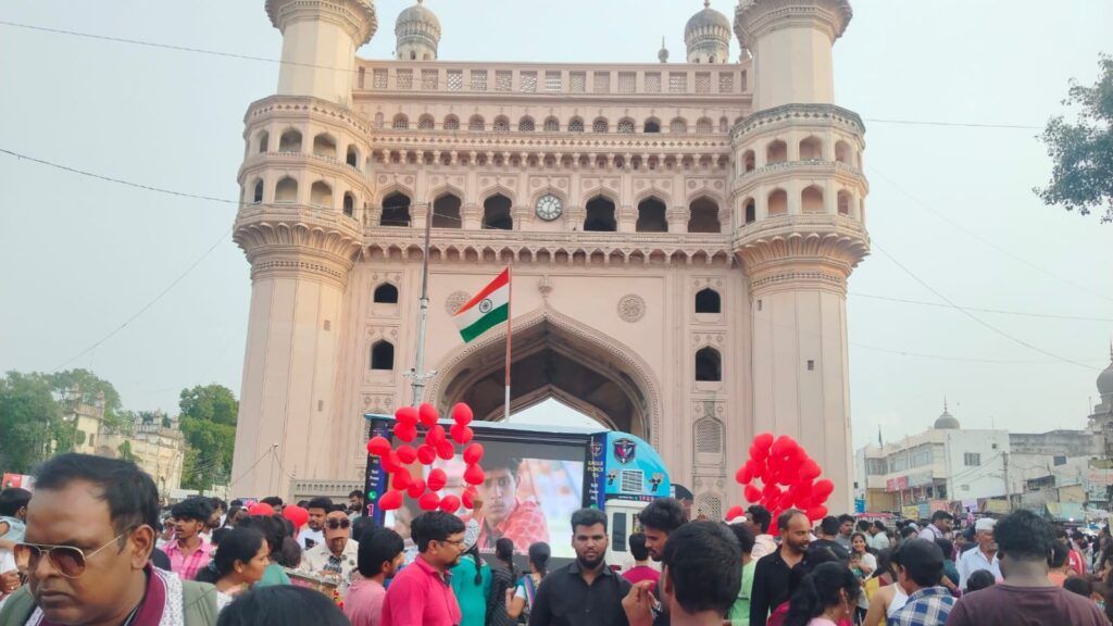 Crowd gathered at Charminar in Hyderabad during a celebration with balloons and flags.