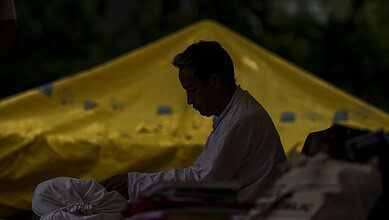 Man sitting outdoors under a yellow canopy, looking down, in a contemplative pose.