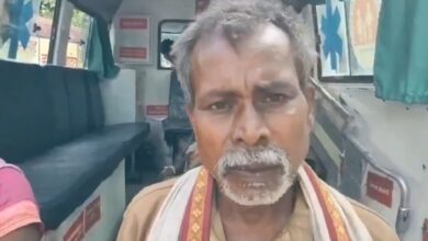 Man with a serious expression inside an ambulance, wearing a traditional shawl.