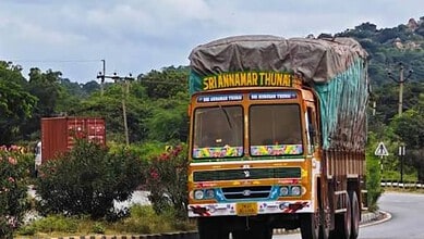 Colourful truck with a covered cargo area on a curved road in a rural area.