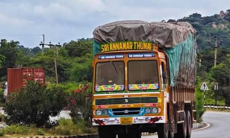 Colourful truck with a covered cargo area on a curved road in a rural area.