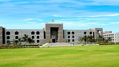 Modern government building with a large green lawn and palm trees in front, under a blue sky.