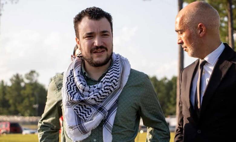 Young man with a beard and scarf talking to a bald man in a suit outdoors.