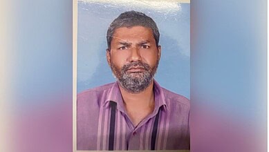 Portrait of a man with a beard wearing a purple shirt against a blue background.