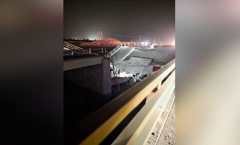Night view of a damaged bridge and water plant with emergency lights and construction activity.