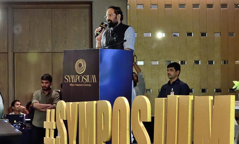 Uttam at the symposium speaking at a podium with the hashtag #SYMPOSIUM and a large golden sign.