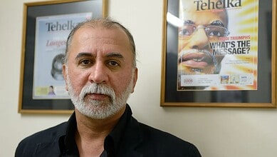 Man with grey beard and black shirt in front of magazine covers at Tehelka office.