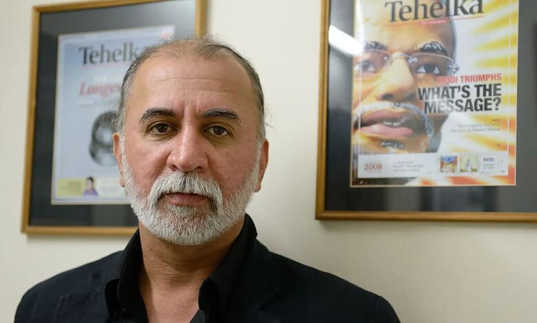 Man with grey beard and black shirt in front of magazine covers at Tehelka office.