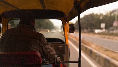 Auto rickshaw driver driving on a highway during daytime in India.