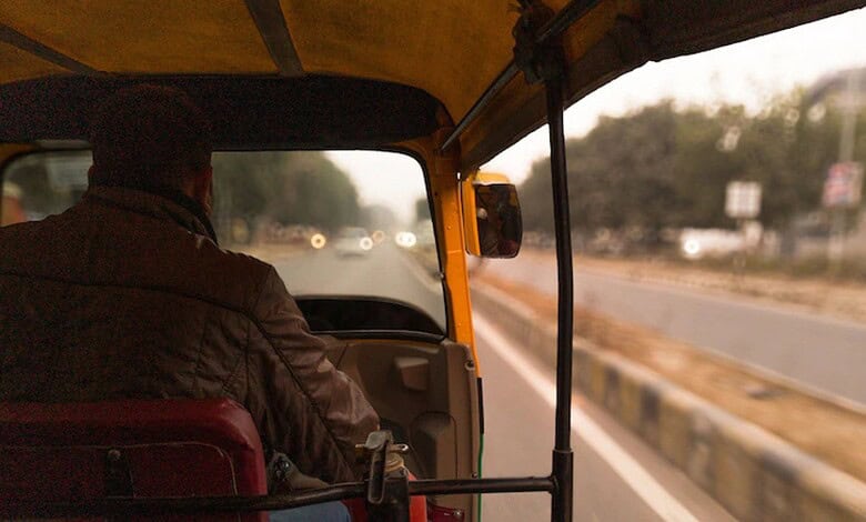 Auto rickshaw driver driving on a highway during daytime in India.