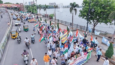 Citizens gather along a riverbank holding flags and banners in a peaceful protest or celebration.