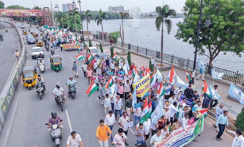 Citizens gather along a riverbank holding flags and banners in a peaceful protest or celebration.
