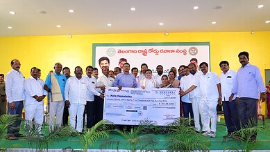 Group of men on stage holding a large cheque at a community event in Telangana.