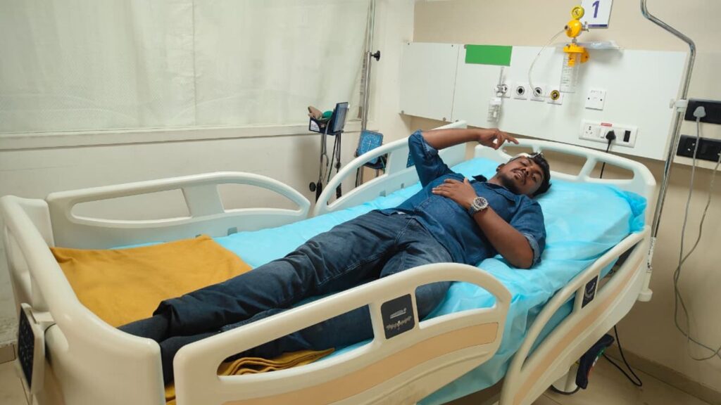Man lying in hospital bed with medical equipment in the background.