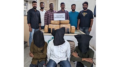 Six men with masked individuals in front, seized drugs and cash on table, crime bust image.
