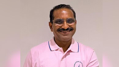 Smiling man in pink shirt with glasses, indoor setting, professional appearance.