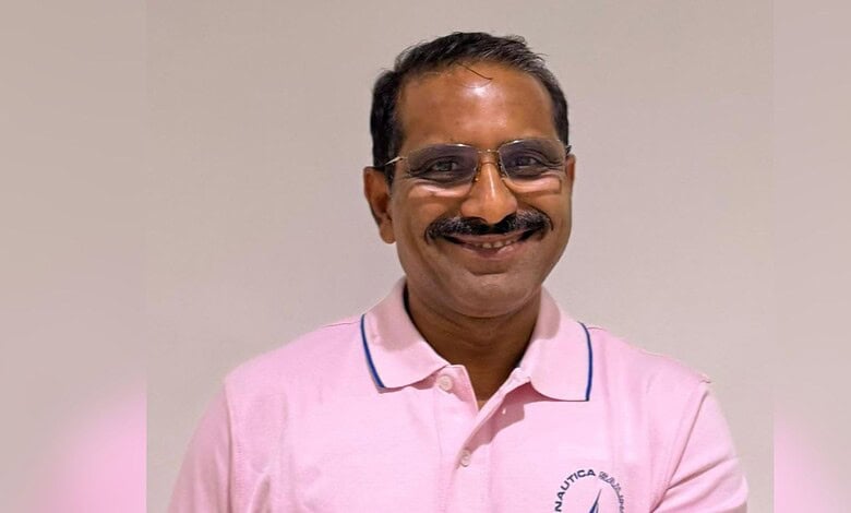 Smiling man in pink shirt with glasses, indoor setting, professional appearance.