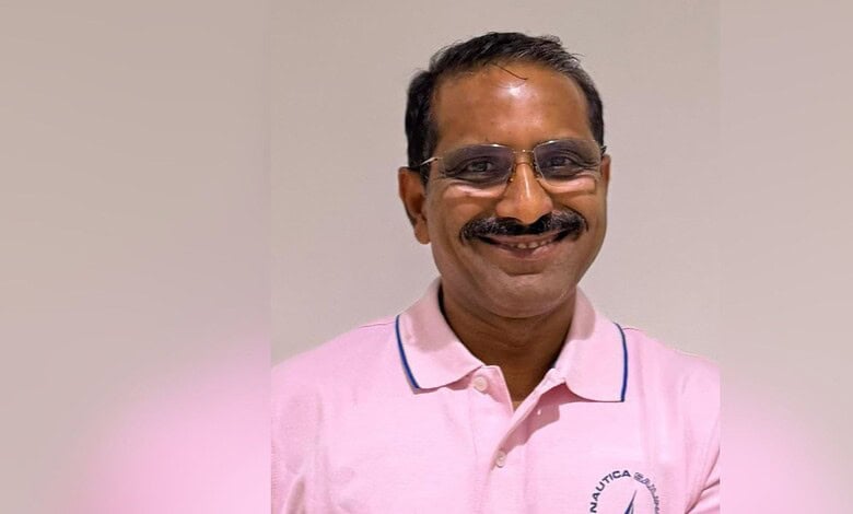 Smiling man with glasses and moustache wearing a pink shirt in an indoor setting.