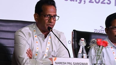 Naresh Pal Gangwar speaking at a conference with a microphone and water bottle on the table.