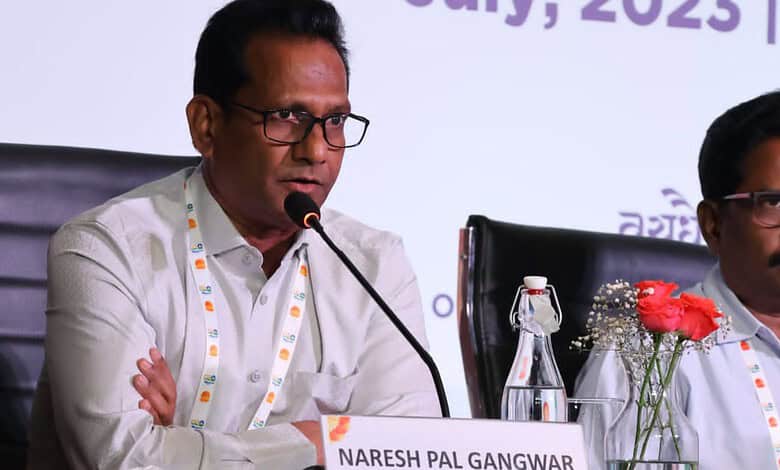Naresh Pal Gangwar speaking at a conference with a microphone and water bottle on the table.