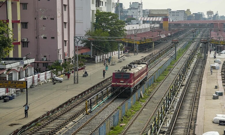 Electric train on railway tracks in an urban setting with buildings and station platform.
