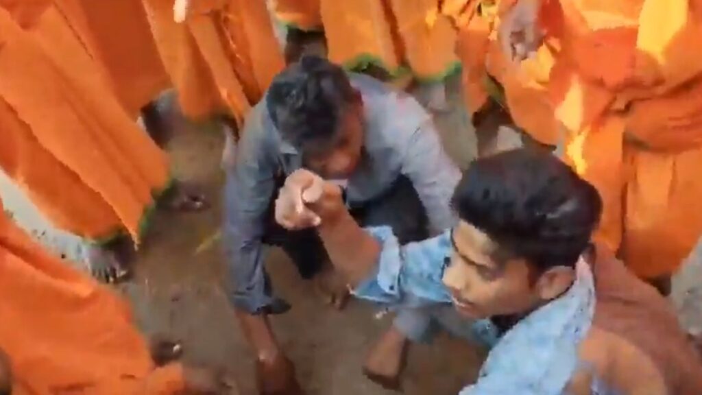 Two young men engaging in an arm wrestling match surrounded by a crowd in orange attire.
