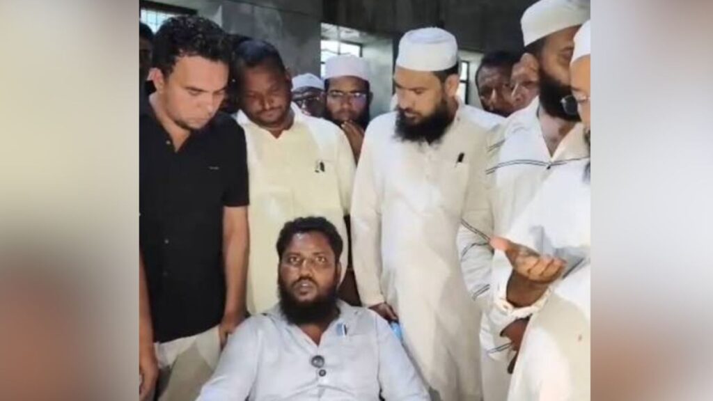 Group of men, some in traditional attire, gathered around a seated man in a white shirt.