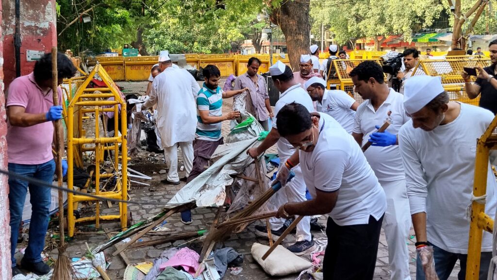 People cleaning debris and repairing at Jantar Mantar during a protest recovery effort.