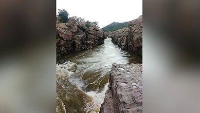 River flowing between rocky cliffs with greenery in the background.