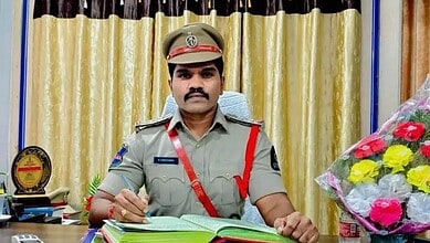 Malakpet SI in uniform at desk with flowers and awards in background.