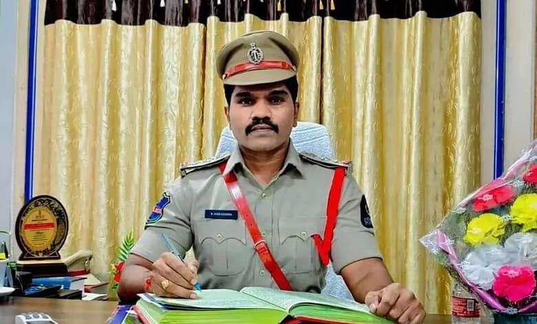 Malakpet SI in uniform at desk with flowers and awards in background.