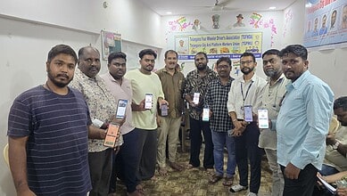 Group of men holding smartphones at a community event in a room with banners.