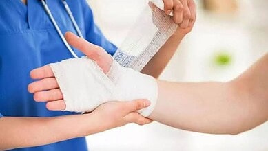 Medical professional bandaging a patient's hand in a clinical setting.