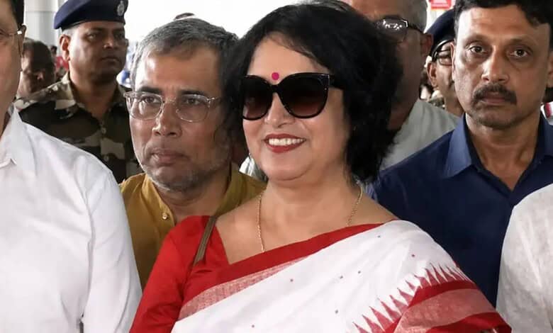 Taslima Nasreen in a white saree with red border, wearing sunglasses, smiling among a crowd in Kolkata.