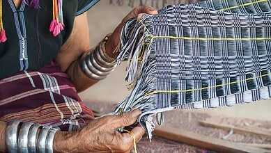 Weaver working on handloom with colourful threads in a traditional setting.