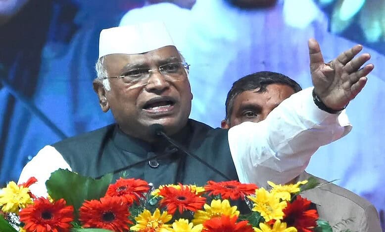 Karnataka politician speaking passionately at a public event with flowers in front.