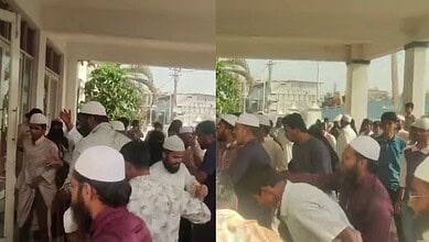 Crowd gathered outside a building during daytime, some wearing traditional caps.