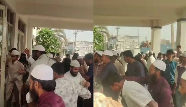 Crowd gathered outside a building during daytime, some wearing traditional caps.