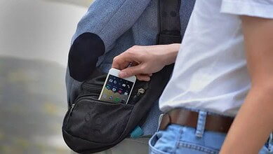 Person placing a smartphone into a black waist bag at an outdoor setting.