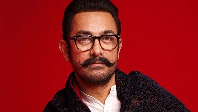 Aamir Khan with glasses and a moustache against a red background.