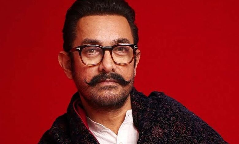 Aamir Khan with glasses and a moustache against a red background.