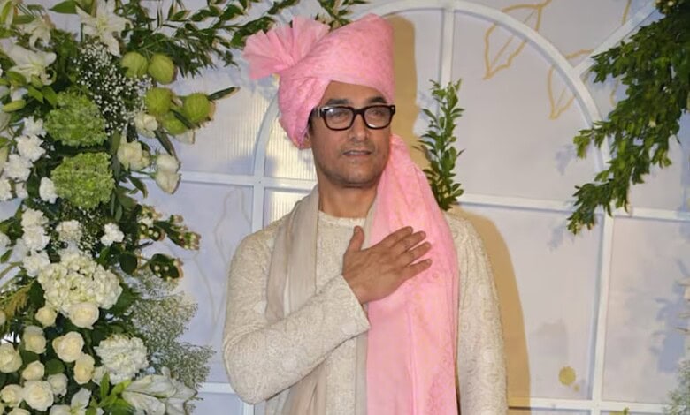 Indian man in traditional attire with pink turban and glasses at a wedding event.