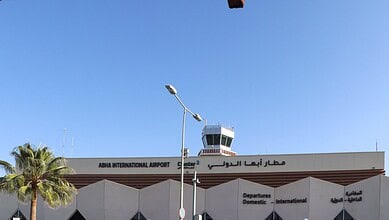 View of Abha International Airport control tower with clear blue sky and palm trees.
